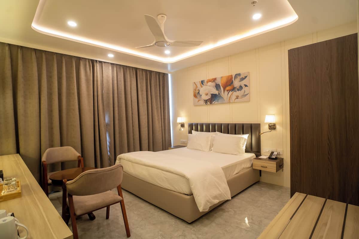 A hotel room with a bed, a desk with a chair, a nightstand with a lamp, and a ceiling fan.