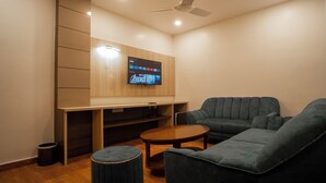 A modern living room with a flat-screen TV mounted on the wall, a ceiling fan, and a dark green sofa.