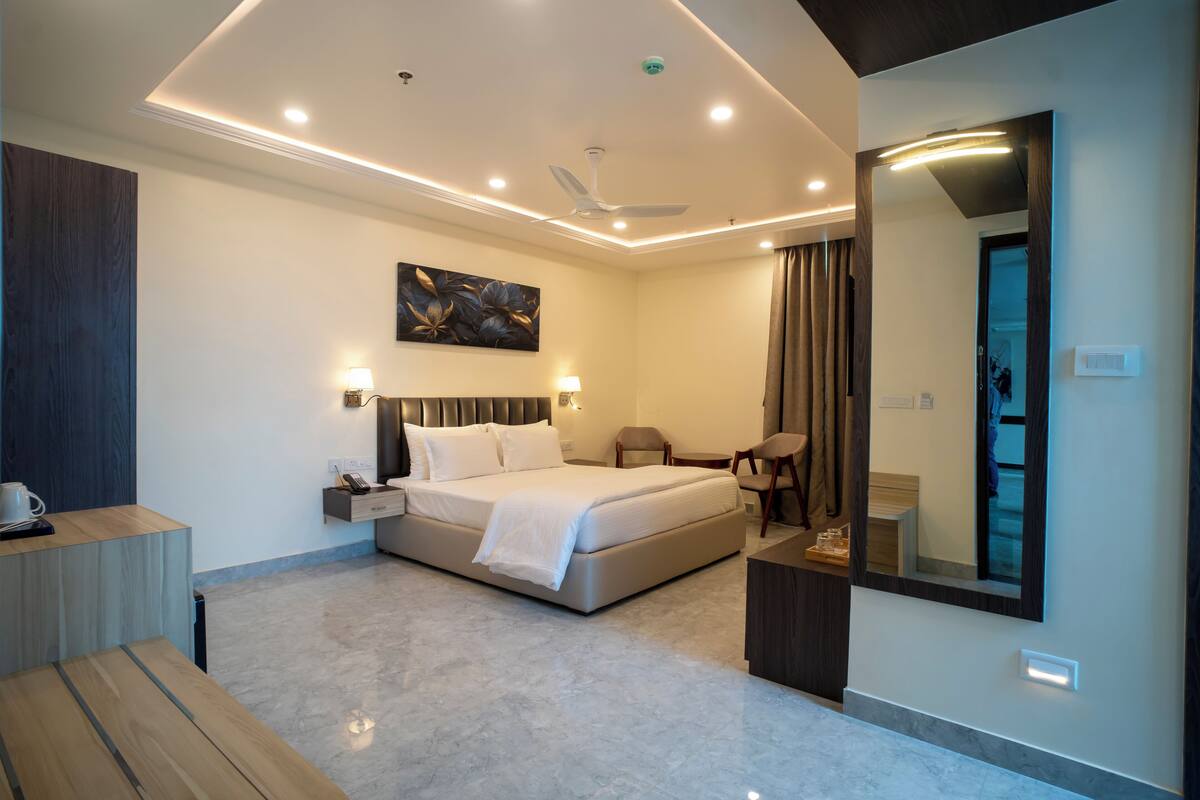 A modern hotel room with a large bed, bedside tables, a desk, and a mirror.