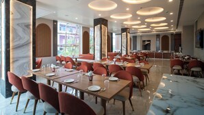 A spacious dining area with multiple tables and chairs, large windows, and modern ceiling lighting.