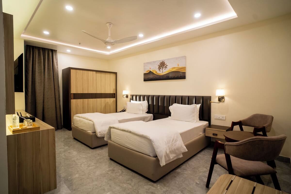 A hotel room with two beds, a desk, a chair, a TV, and a ceiling fan.