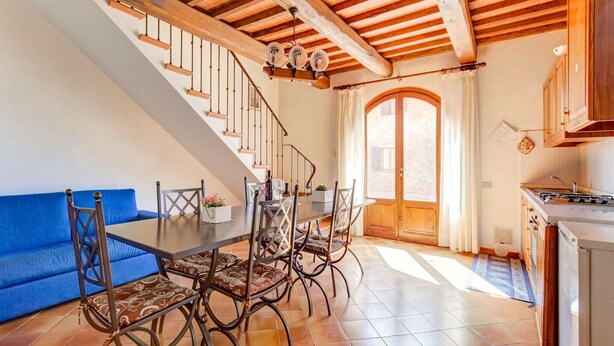 Un comedor amplio con una escalera de madera, un sofá azul y una zona de cocina con estufa.