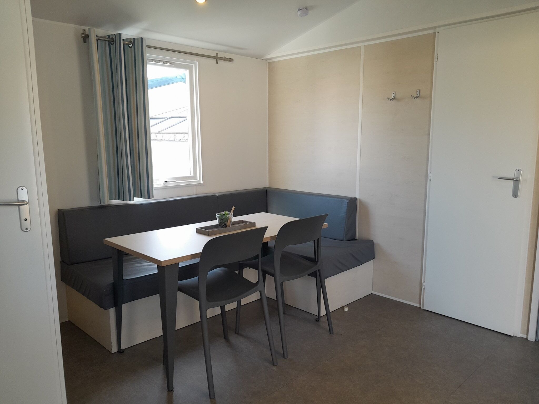 A small room with a single table and two chairs, a window with curtains, and a door.