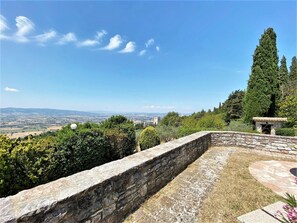 A stone retaining wall with a stone building in the background, surrounded by greenery and a clear view of the landscape. - Elegant Retreat in Umbria (Assisi)