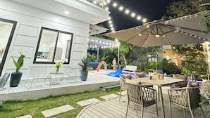 Een modern terras buiten met een eethoek, een zwembad en een overdekte zithoek.