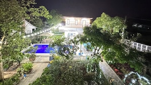 Een tweelaags huis met een zwembad en een verlichte tuin 's nachts.