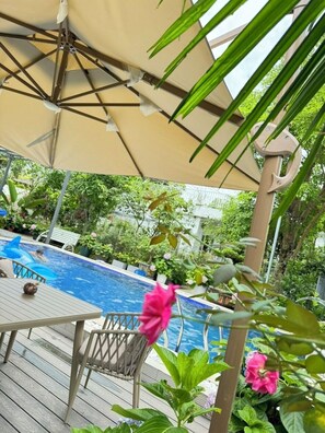 Un espace extérieur avec une piscine, une terrasse en bois, une table ornée d’une coquille de noix de coco et une chaise.