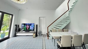 Een moderne woonkamer met een grote televisie, een eethoek en een trap.