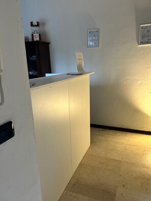 Un mostrador de recepción con encimera blanca, un aviso en el muro y un mueble pequeño con objetos encima.