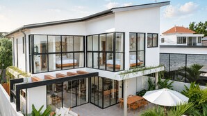 Una casa moderna con balcón de cristal, piscina y mobiliario exterior.