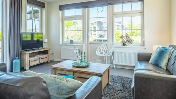 Una sala de estar con televisión, sofá, mesa de centro y ventanas amplias.