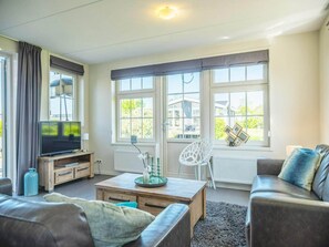 A living room with a TV, sofa, coffee table, and large windows.
