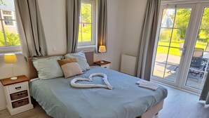 Un dormitorio con cama, mesita de noche, lámpara, ventana y vistas al exterior.