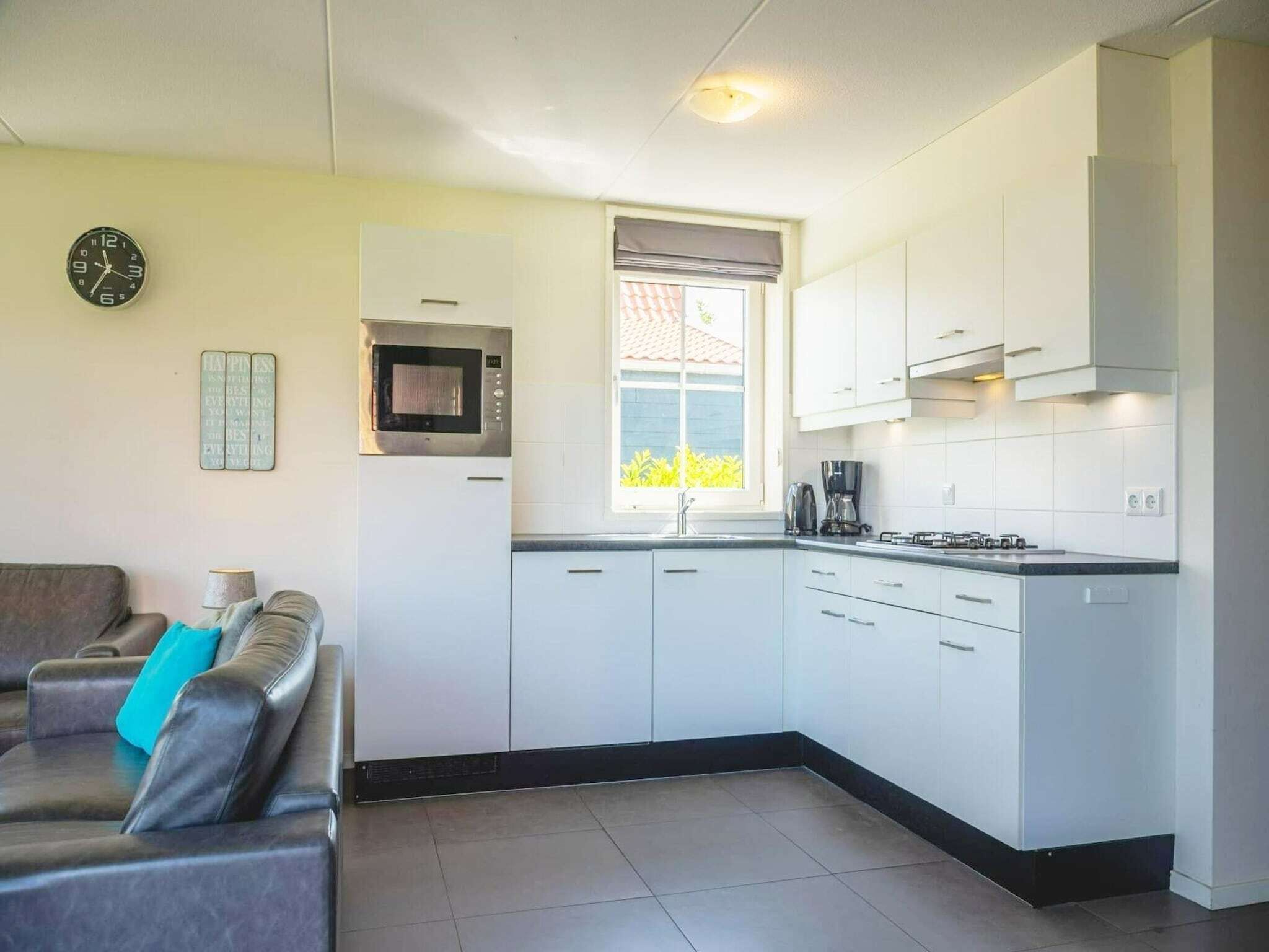A modern kitchen with white cabinets, a built-in microwave, a window with a view, and a clock on the wall.
