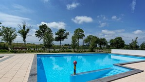 Una piscina rectangular al aire libre con una superficie de agua azul cristalina, rodeada por un solárium con baldosas.