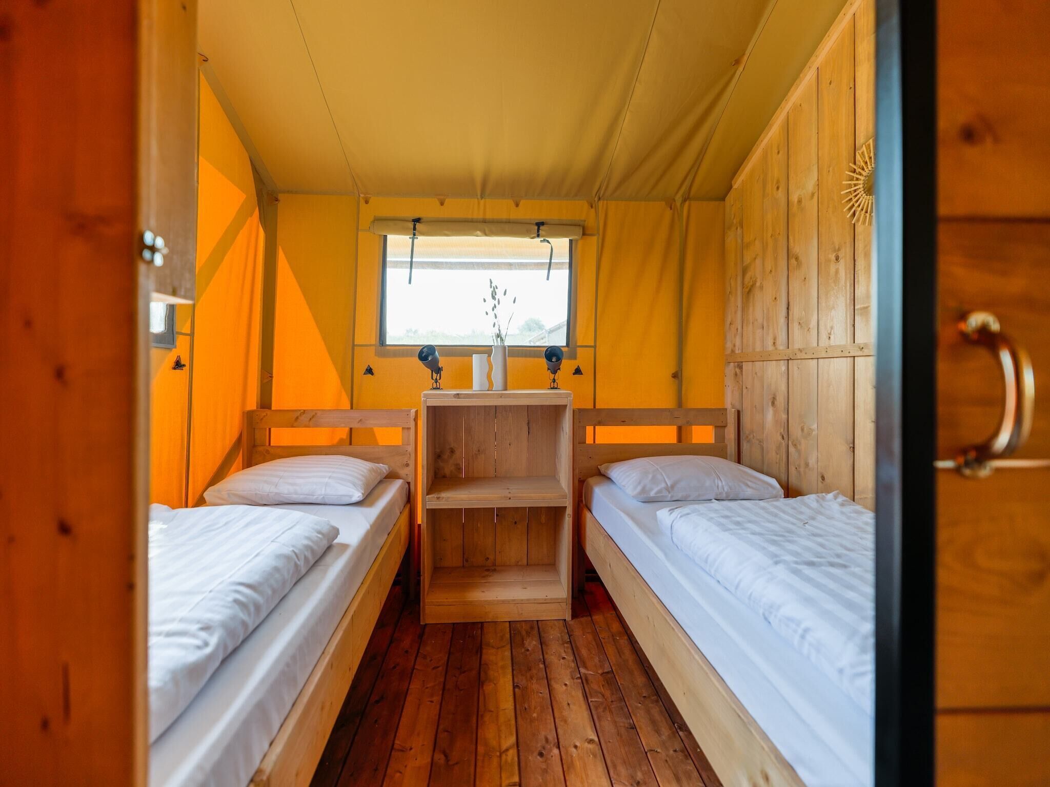 A compact room with two wooden beds, a small table, and a window with a view.