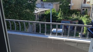 Un balcó amb sòl de rajola, barana blanca i vista a una zona residencial amb arbres i edificis.