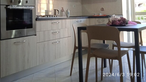 Una cuina moderna amb electrodomèstics integrats, armaris de fusta i zona de menjador amb taula i cadira.