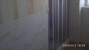 Bany amb parets de rajola blanca i una cabina de dutxa de vidre.
