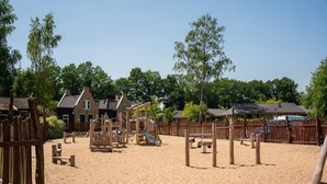 Une aire de jeux sablonneuse avec des structures de jeu en bois et une clôture.