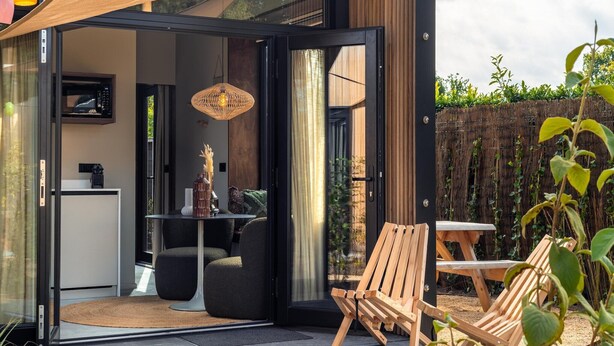 Un espace extérieur moderne aménagé avec des sièges, une porte d’entrée en verre, une chaise en bois et une table.