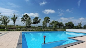 Ein rechteckiger Pool im Freien mit blauer Wasseroberfläche, umgeben von einer gefliesten Terrasse.