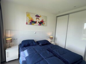 A bedroom with a bed, two bedside tables, a wall-mounted painting, and a sliding closet door.
