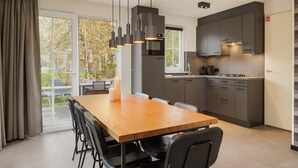 A modern kitchen with dark cabinets, a wooden dining table, and black chairs. - Home w/ Sauna & Garden (Bad Bentheim)