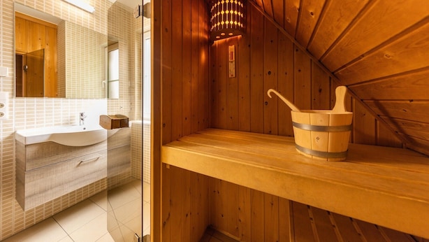 A sauna room with wooden walls, a wooden bench, and a wooden bucket with a handle.