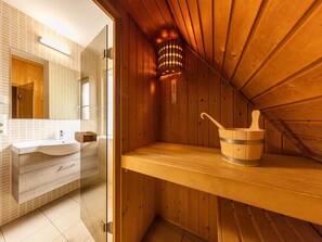 A sauna room with wooden walls, a wooden bench, and a wooden bucket with a handle.