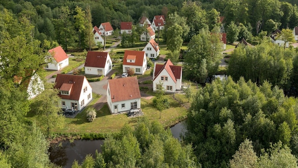 Et boligområde med hvide huse og røde tage, omgivet af frodig grøn vegetation og et mindre vandareal.