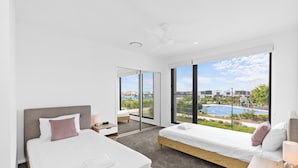 Une chambre moderne avec deux lits, une grande fenêtre donnant sur une piscine et des bâtiments, et un ventilateur de plafond.
