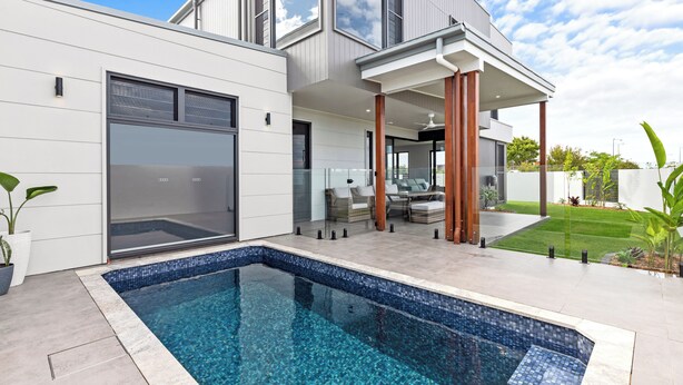 Une maison moderne dotée d’une piscine, de grandes fenêtres et d’un espace extérieur aménagé avec un coin salon couvert.