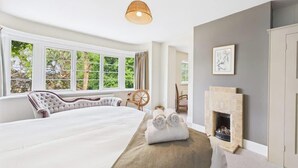 A bedroom with a large bed, a fireplace, a window with curtains, and a hanging light fixture.
