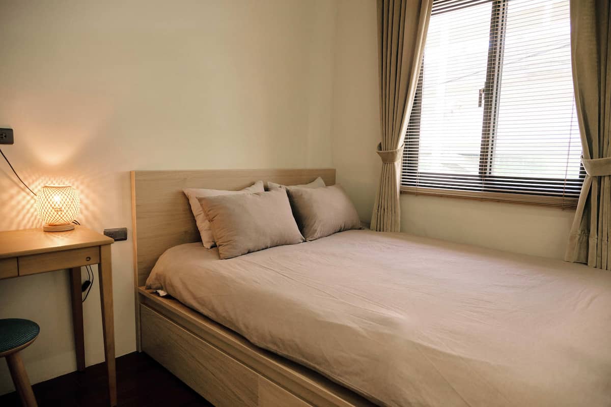 A single bed with a wooden headboard, a bedside table with a lamp, and a window with curtains.