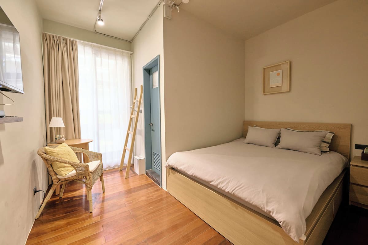A bedroom with a bed, a chair, a desk, and a ladder.