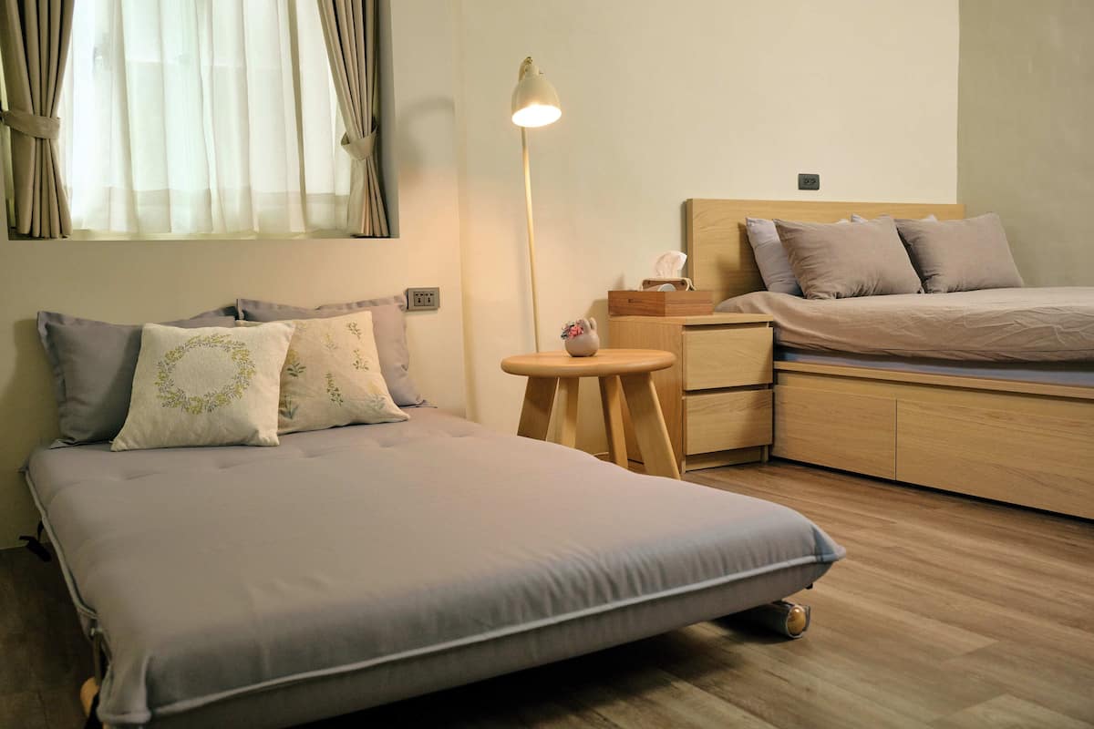 A bedroom with a bed, bedside table, lamp, and a small stool.