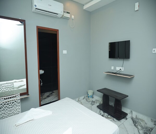 A modern bathroom with a bed, a toilet, a shower, a sink, and a mounted TV.