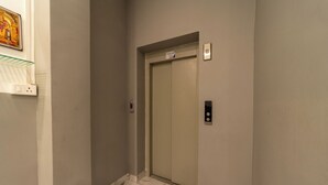 Un ascensor en un pasillo con piso de mármol, un interruptor de luz en la pared y un detector de incendios.