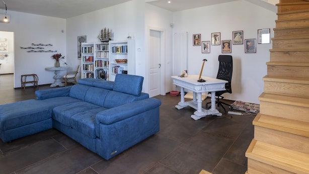 A spacious living room with a blue sectional sofa, a white bookshelf, and a staircase. - Our Dream by Interhome (Alassio)