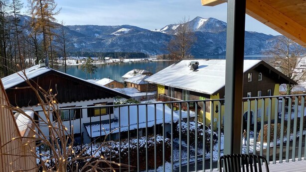 A balcony with a view of a lake, snow-covered buildings, and mountains in the background. - Deluxe One-Bedroom Apartment with Lake View (Sankt Wolfgang im Salzkammergut)