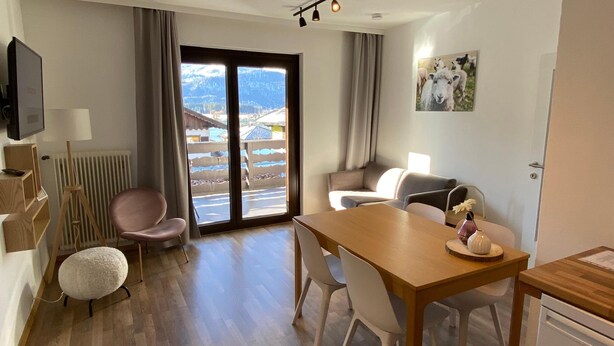 Ein modernes Hotelzimmer mit einem Holztisch, einer Couch und einem Stuhl. Ein großes Fenster bietet Blick auf Berge und einen Pool.