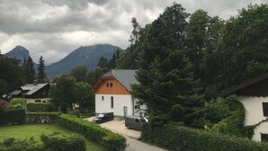 Ein kleines, eingeschossiges Gebäude mit einem geneigten Dach, umgeben von üppiger Vegetation und einem Berg im Hintergrund.