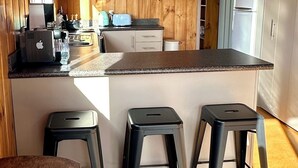 A modern kitchen with wooden paneling, a central island with stools, and built-in appliances. - Yasmin Cottage - for an instant holiday feel.  (Kinloch)