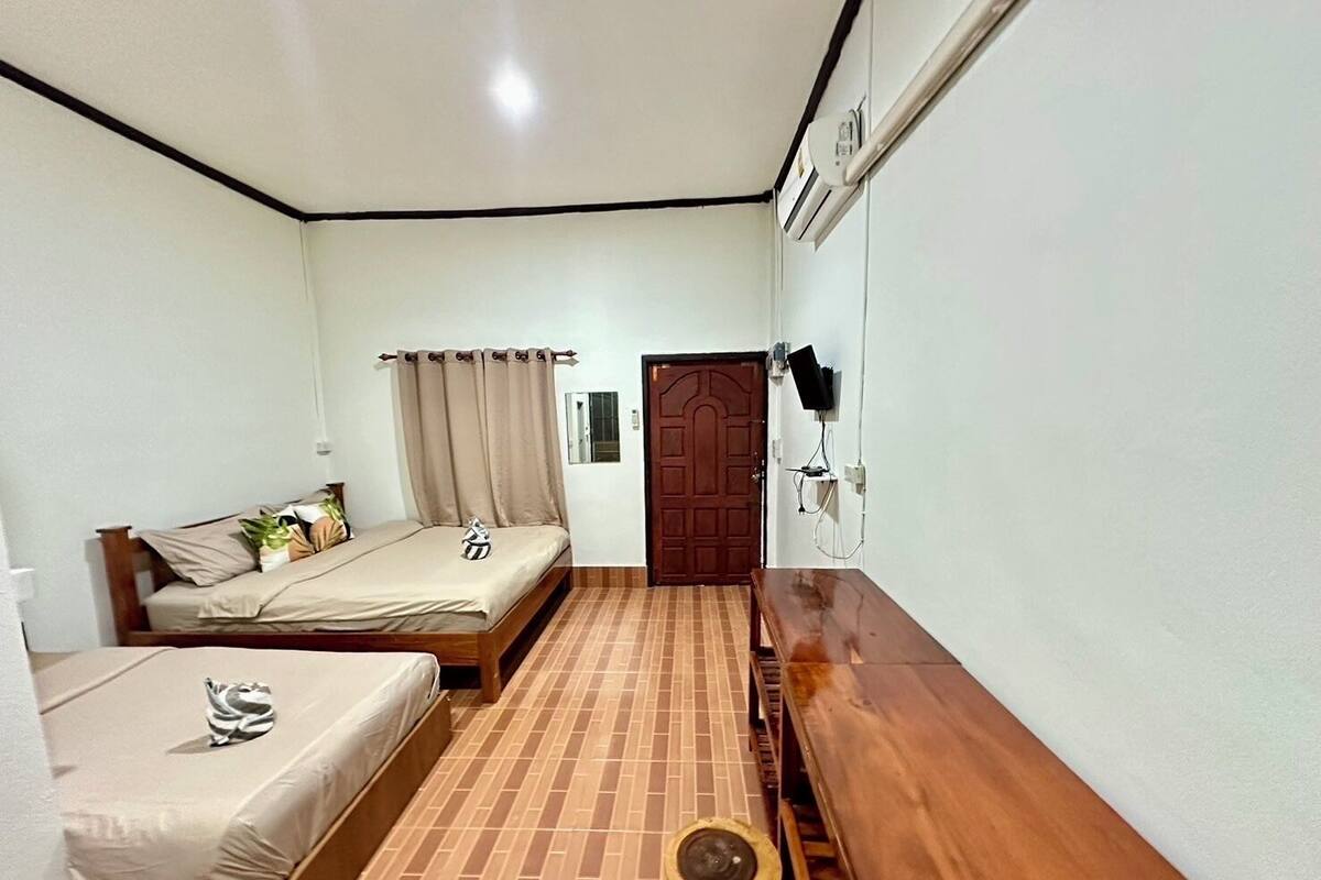Quarto compacto com cama, uma mesinha, um banquinho e uma porta.