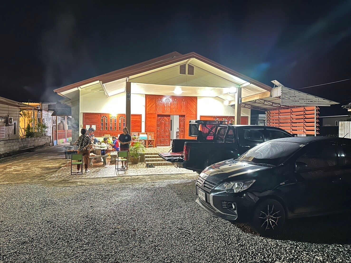 Ein Gebäude mit einer überdachten Terrasse, ein schwarzes Auto davor geparkt und ein Lastwagen im Hintergrund.