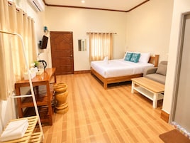 A hotel room with a bed, a sofa, a wooden table, a desk, a chair, a TV, and a door.