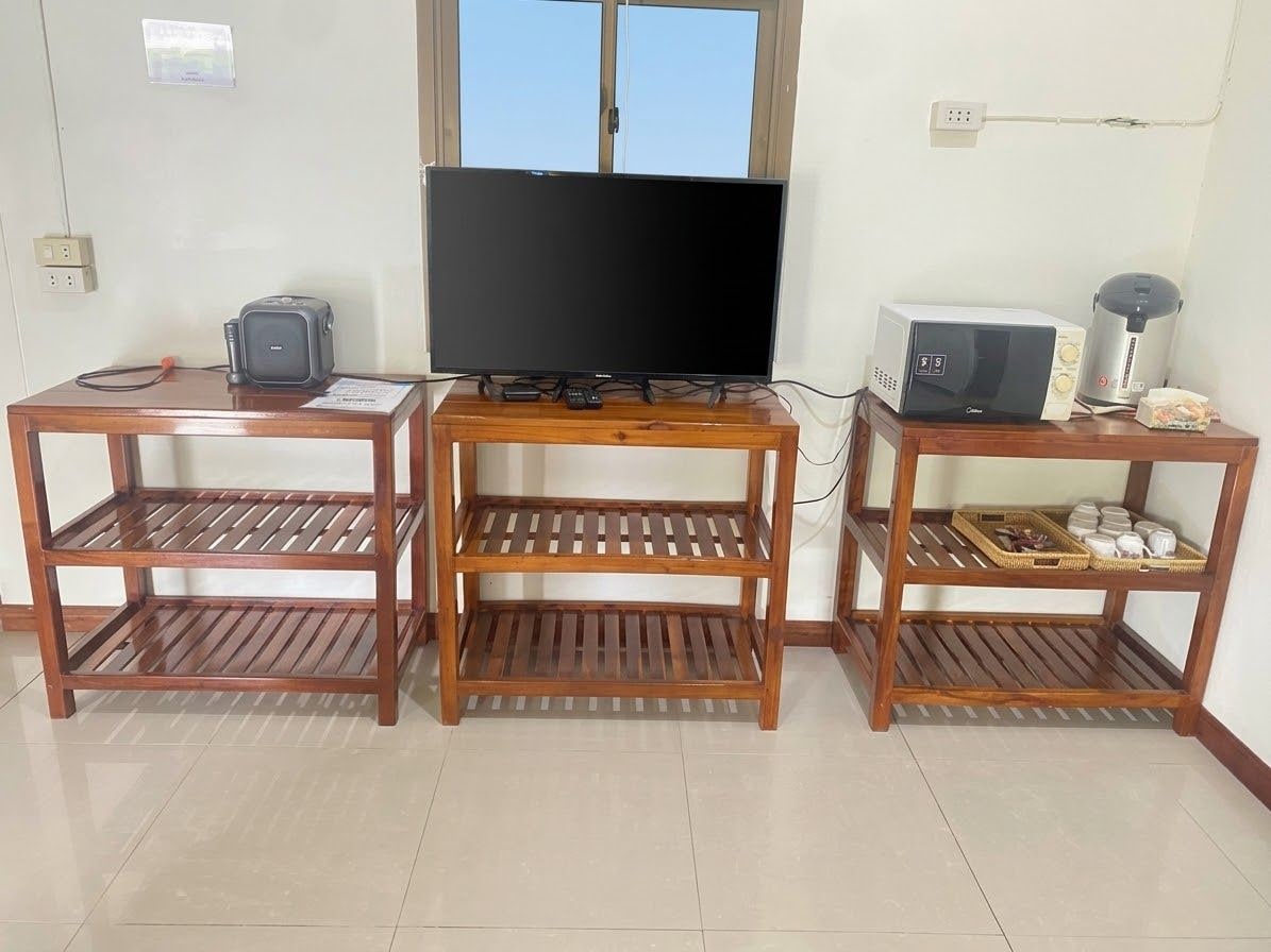 A room with a television on a wooden stand, a microwave, and a toaster on separate wooden tables.