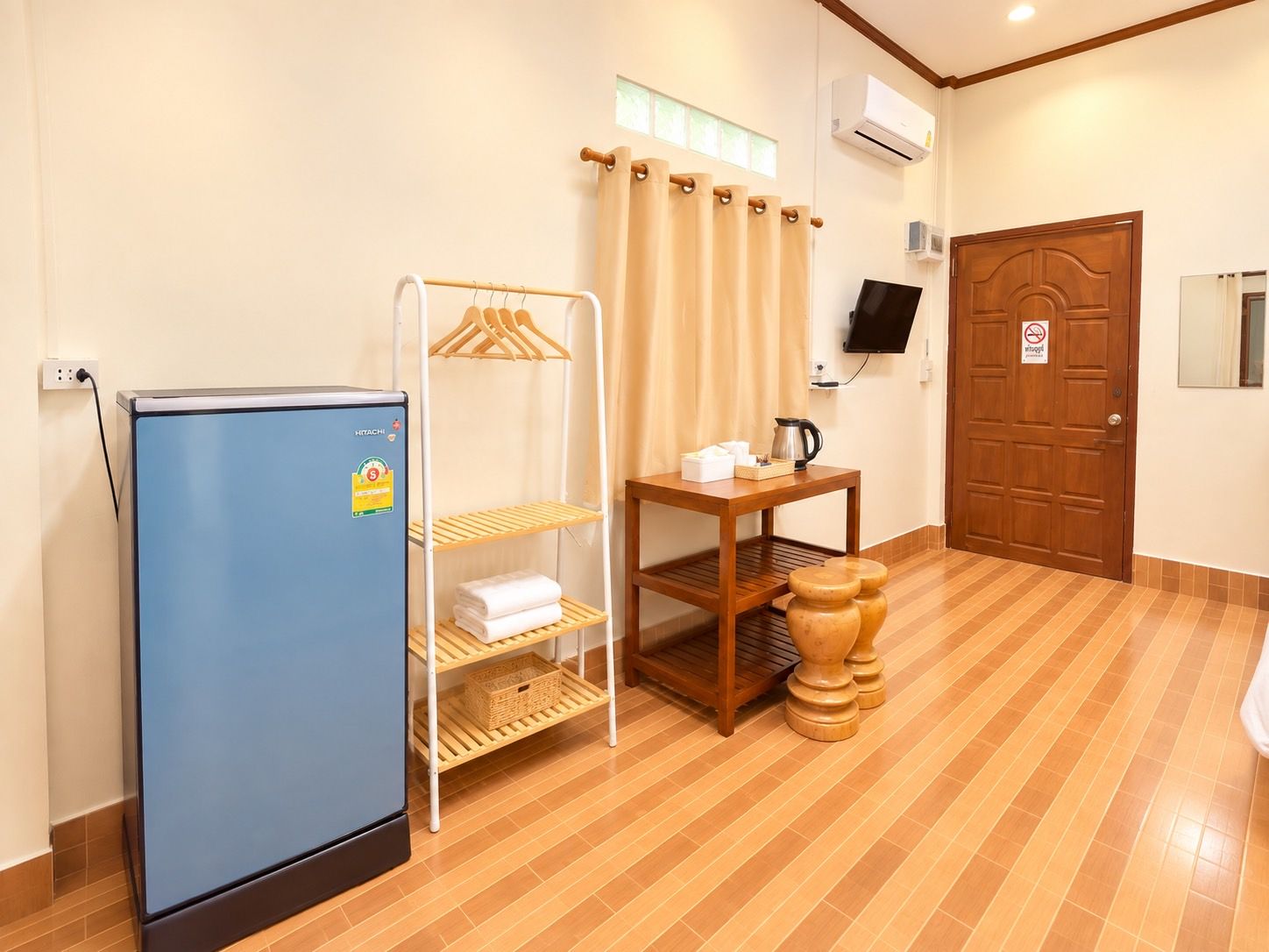 A hotel room with a minibar, a wooden table with a kettle, a television, and a door with a no-smoking sign.