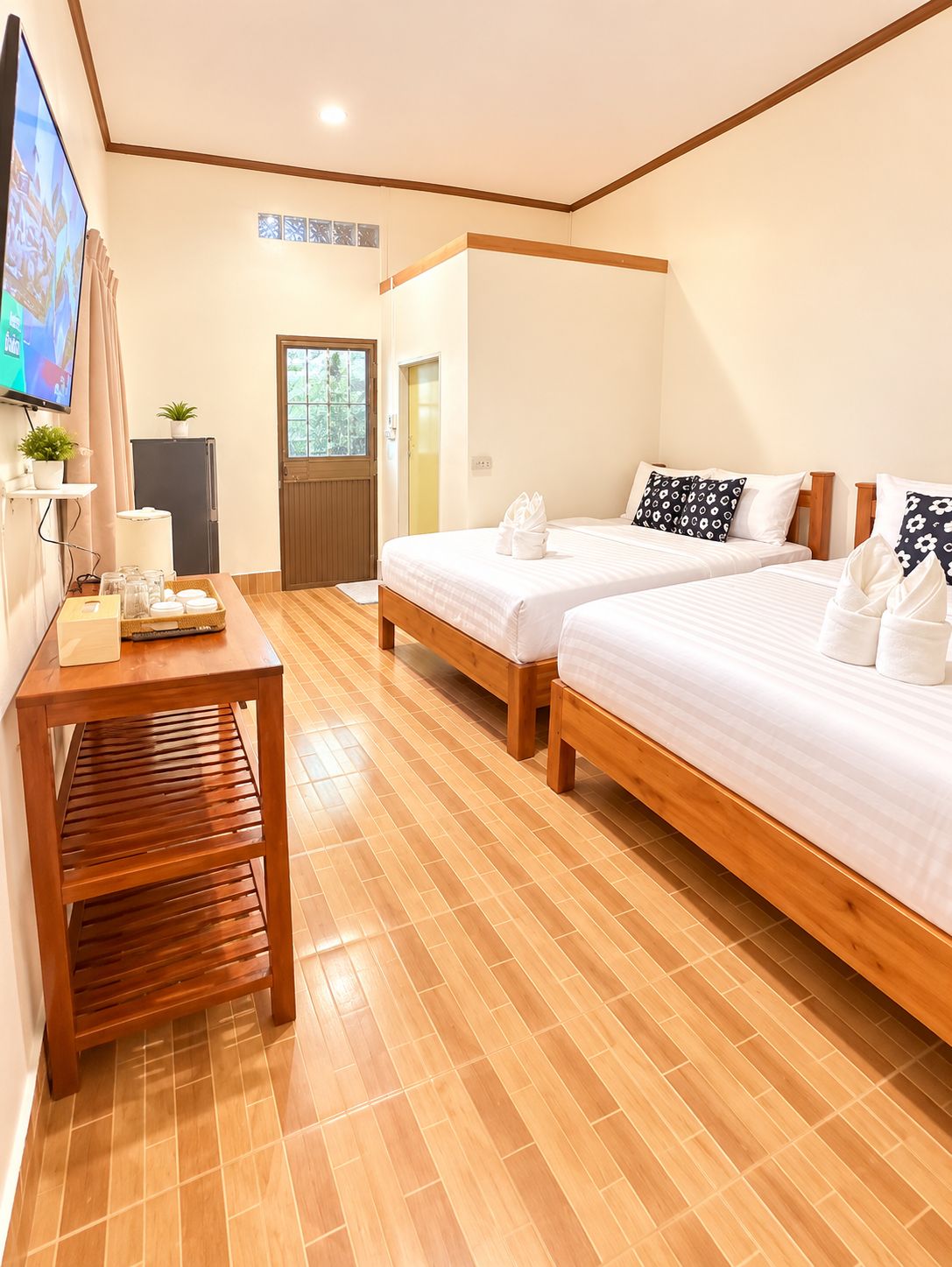 Habitación de hotel con dos camas, una mesa de madera, un televisor y una puerta que da a un balcón.